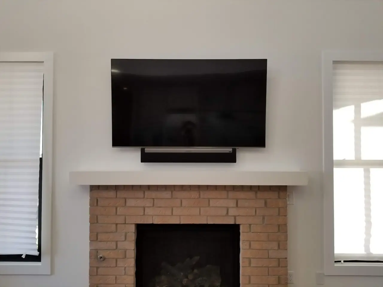 Blonde brick fireplace with a white floating mantel, TV and soundbar centered between two windows