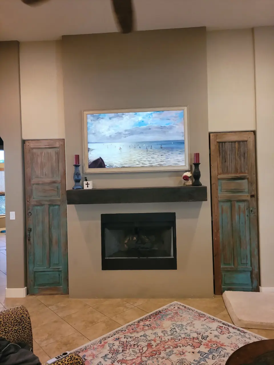 Samsung Frame TV displaying art above a wood mantel, flanked by rustic teal doors